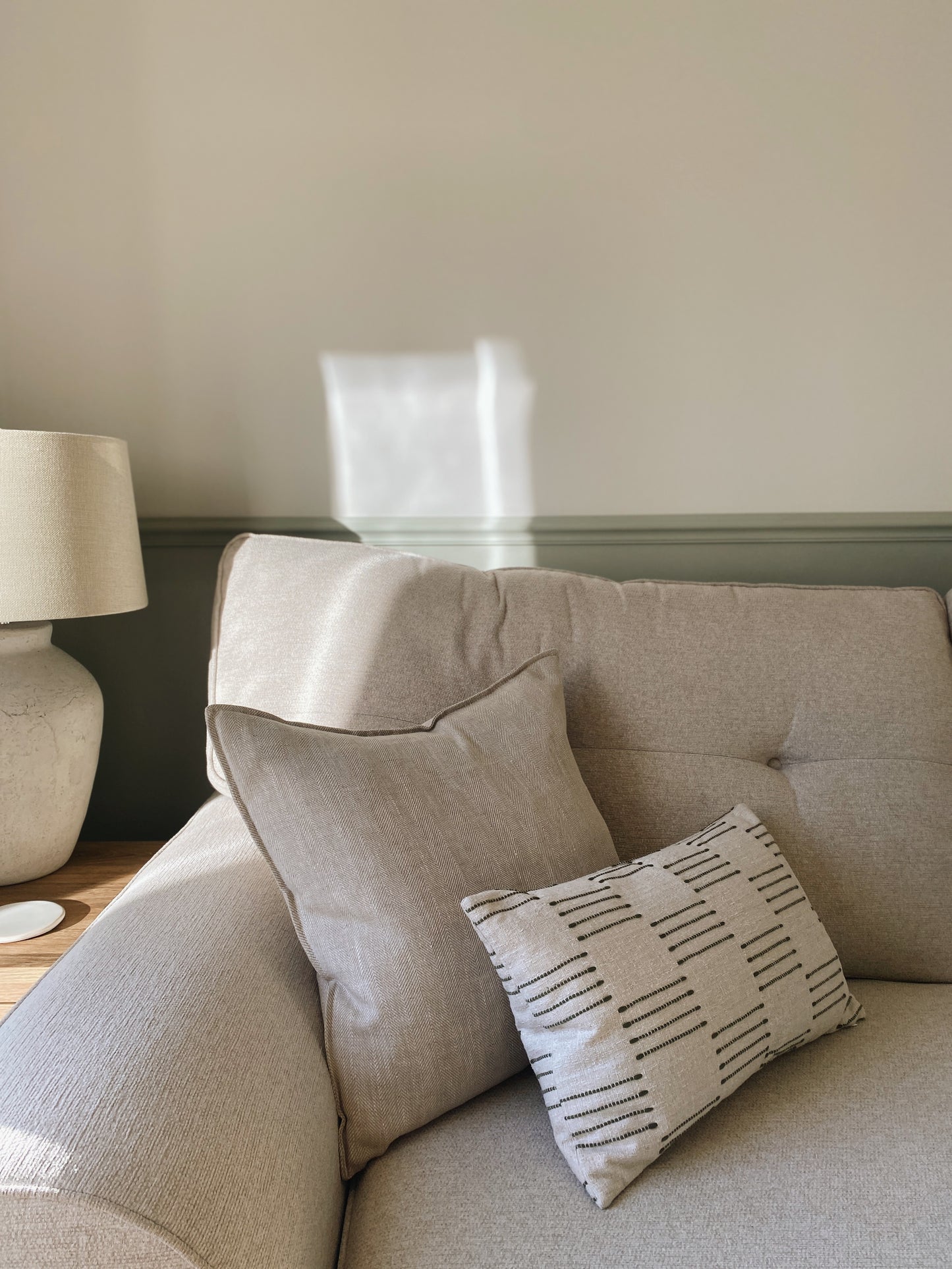Beige sofa with patterned pillow and lamp on wooden table in room.