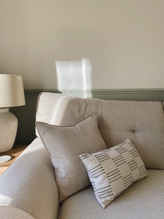 Beige sofa with patterned pillow and lamp on wooden table in room.